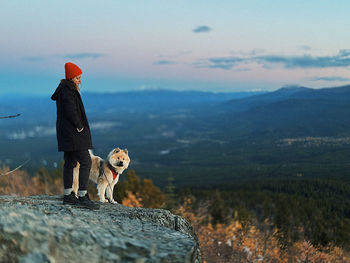 Rear view of woman standing on rock against sky during sunset