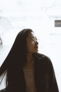 Portrait of smiling young woman standing against window