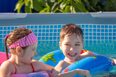 Little girl and little boy play and having fun in kiddie pool at summer sunny day. 
