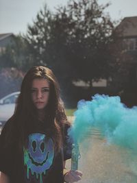Portrait of young woman holding blue distress flare while standing outdoors
