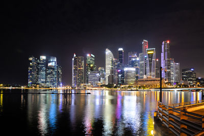 Illuminated buildings by river against sky at night