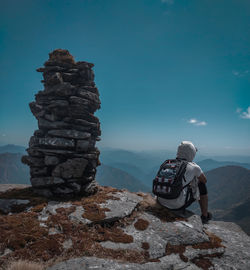 Man sitting on the top of the hill and looking to the mountains under the blue sky.