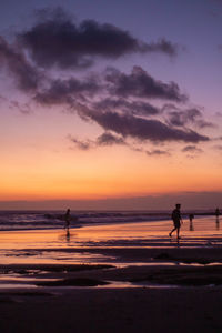 Silhouette people walking on beach against sky during sunset