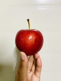 Close-up of hand holding apple against white background