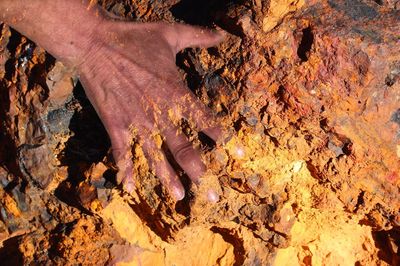 Cropped hand touching rock during sunny day