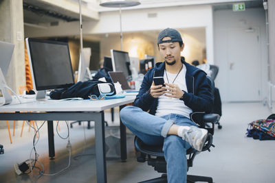 Male computer programmer using smart phone while sitting on chair in office