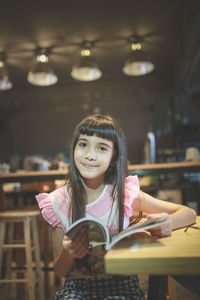 Portrait of girl with book at table in restaurant