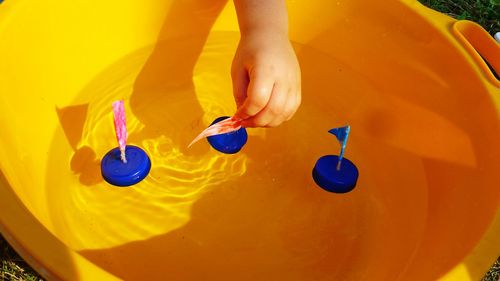 Cropped hand of girl playing with bottle cap in bucket