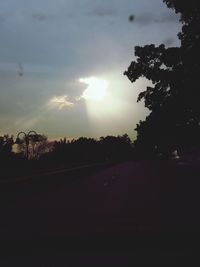 Road amidst silhouette trees against sky during sunset