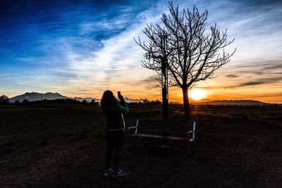 Woman standing by bare tree on landscape against sky