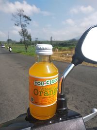 Close-up of orange bottle on road against sky