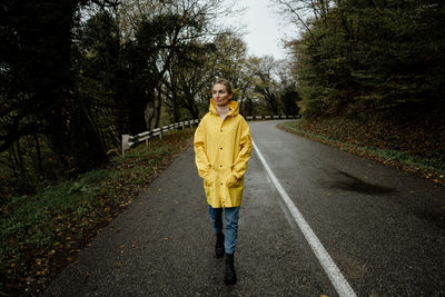 A serene middle-aged woman in a yellow raincoat walks in rainy weather in the countryside.