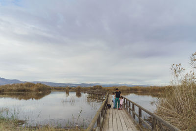 Pier over lake against sky and family walking on a bridge