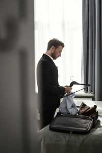 Side view of businessman positioning shirt on coathanger in hotel room