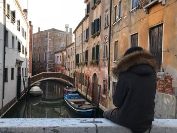 Woman sitting on retaining wall over canal against buildings