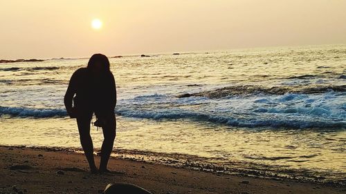 Rear view of woman standing on beach against sunset sky