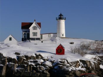 Lighthouse on snow covered hill against sky