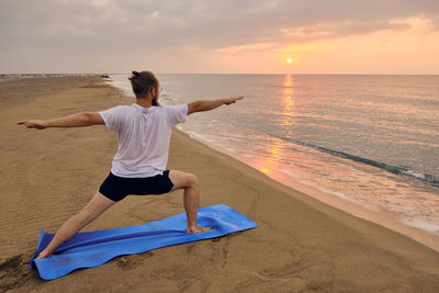 Man doing yoga on beach during sunset