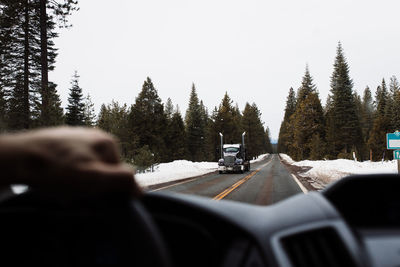 Anonymous traveler driving automobile on asphalt countryside roadway with oncoming truck among coniferous woods in winter day in usa