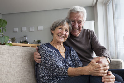 Happy senior couple sitting on the couch in the living room holding hands