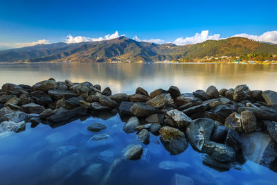 Rocks by lake against blue sky