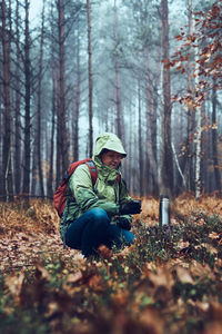 Woman with backpack having break during autumn trip drinking a hot drink from thermos flask