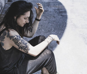 Side view of mature woman with tattoos sitting on footpath