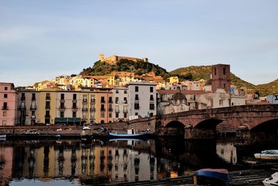 Bridge over river by buildings in city against sky