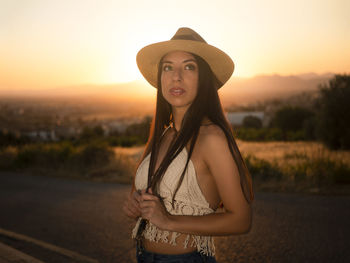 Portrait of young woman standing against sky during sunset