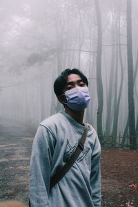 Portrait of young man wearing mask standing against trees
