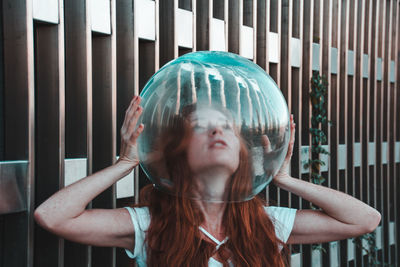 Close-up of young woman removing glass helmet from head against metallic railing