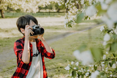 Boy photographing flowering plant outdoors