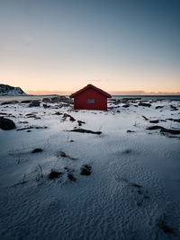 House on snow covered land by building against sky during sunset