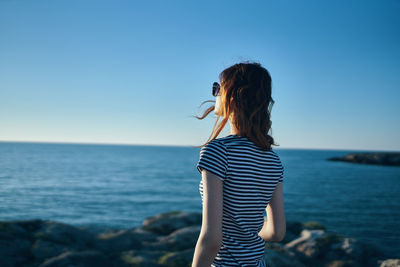 Woman standing in sea against clear blue sky