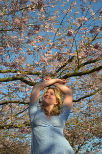 Low angle view of young woman posing against cherry blossom trees.