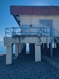 View of abandoned factory by sea against clear blue sky