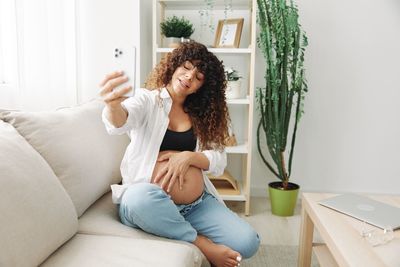 Young woman using phone while sitting on sofa at home