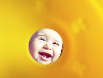 Close-up of cute cheerful baby girl looking through yellow pipe