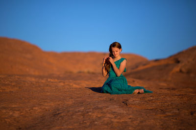 Young woman sitting on rock against clear sky