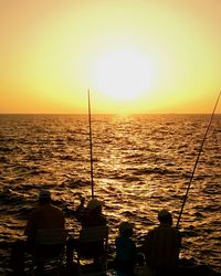 Rear view of silhouette man fishing in sea against sunset sky