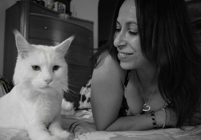 Happy woman looking at cat resting on bed