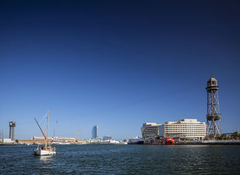 Sailboats in sea by buildings against clear blue sky