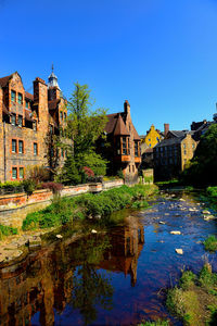 Buildings by lake against clear blue sky