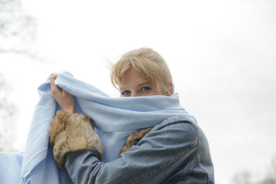 Portrait of woman covering face with scarf against sky