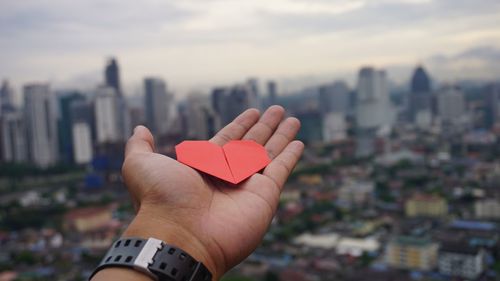 Close-up of hand holding heart shape against cityscape