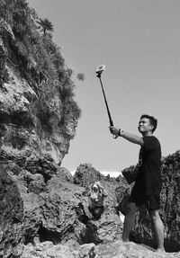 Teenage boy taking selfie with monopod at rocky shore