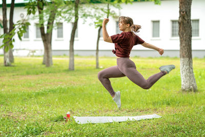 Beautiful girl athlete in sportswear jumps high in the park or in the yard of her house