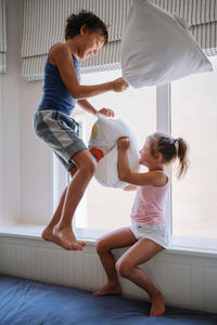 Brother and sister playing at home pillow fight