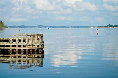 Wooden posts in sea against sky