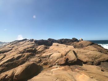 Rock formations by sea against blue sky